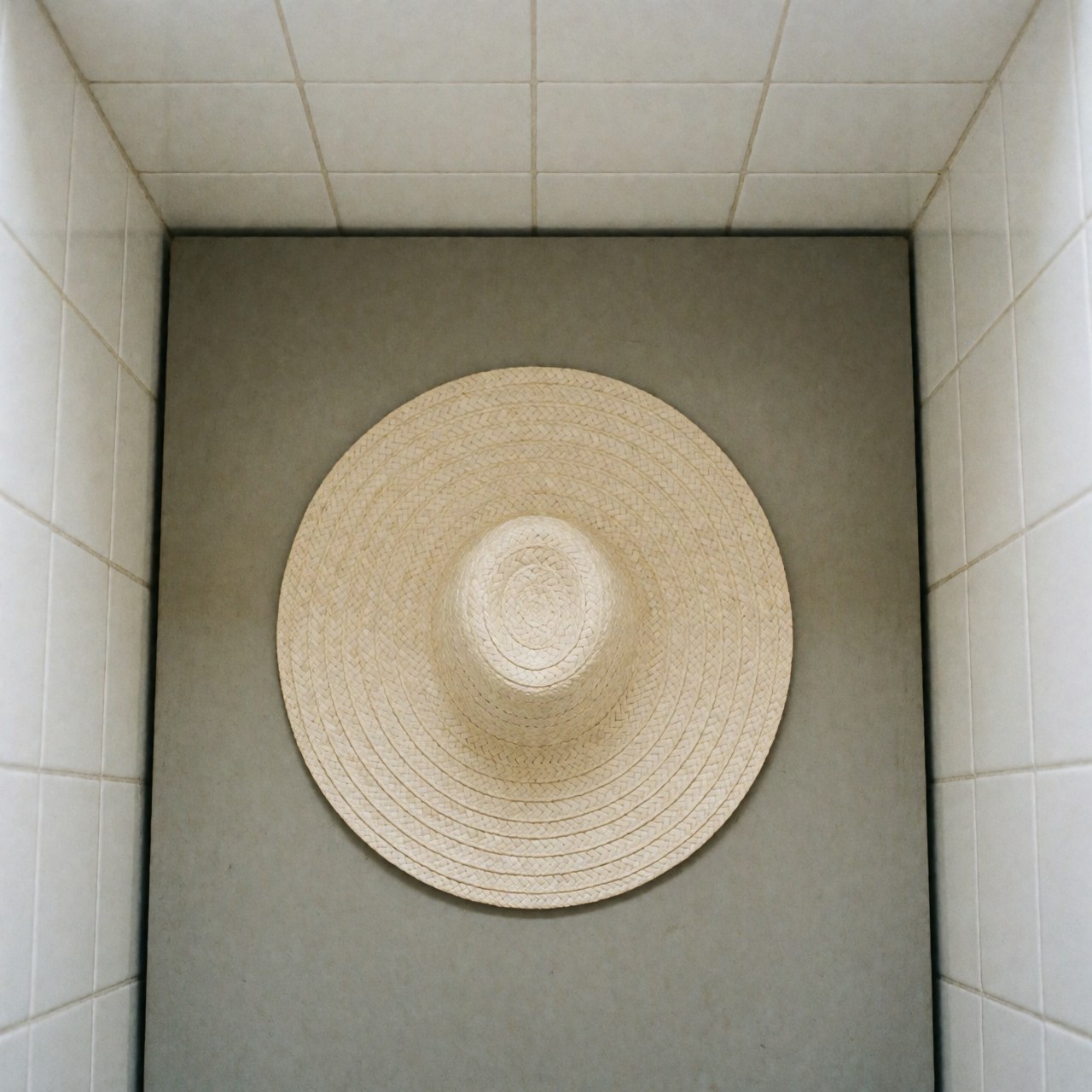 Top view of a traditional Colombian vueltiao straw hat with circular design on a gray surface with white tiled walls and soft lighting
