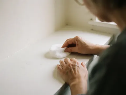 Adult hand holding a white cotton cloth over a clean surface in a beauty studio with natural light and white walls