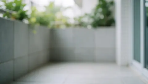 Outdoor balcony background featuring gray tiled walls and floor with blurred green plants, illuminated by soft daylight, ideal for commercial text overlay