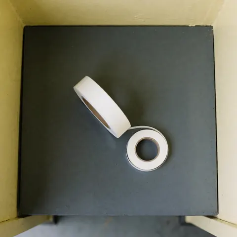 A roll of matte white PTFE tape resting on a gray table, suitable for washing machine repair tasks with soft lighting and a clean background.