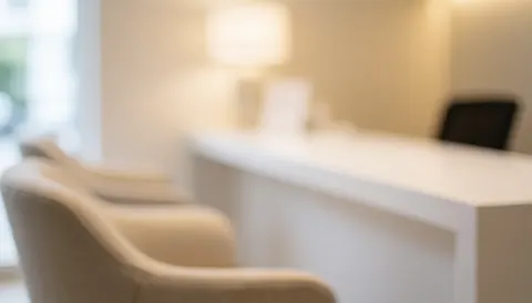 Soft focus background of a serene clinical reception area featuring a white counter and comfortable seating with warm lighting, ideal for text overlays.