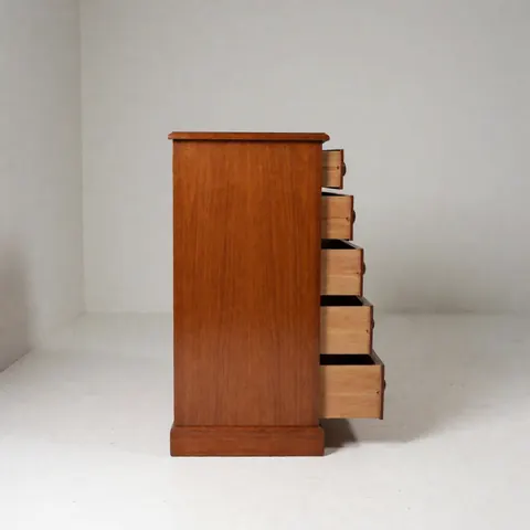 Close-up of an antique wooden cabinet with several open drawers revealing the interior, placed on a white floor against light gray walls with soft lighting.