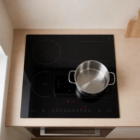 Top view of an empty stainless steel pot placed on a black induction cooktop with a light wood countertop and beige walls