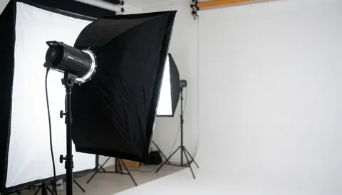 Professional video recording studio featuring softbox lighting, a seamless white curved backdrop, and lighting equipment in the foreground.