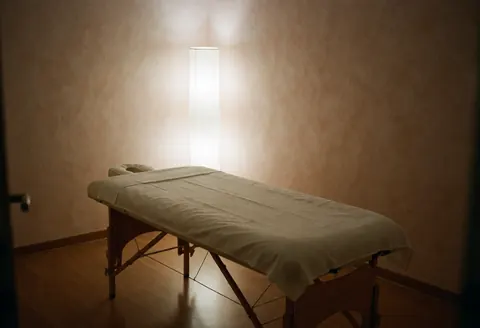 Empty massage treatment room featuring a table, terracotta walls, and soft lamp light creating a calm, clean atmosphere.