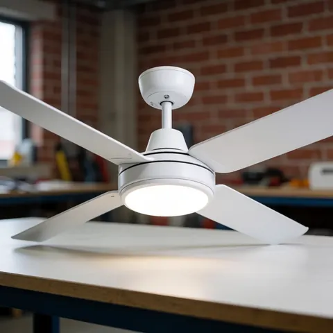 Modern white fan with integrated LED light resting on a workbench in a workshop with a red brick wall and neutral professional lighting.