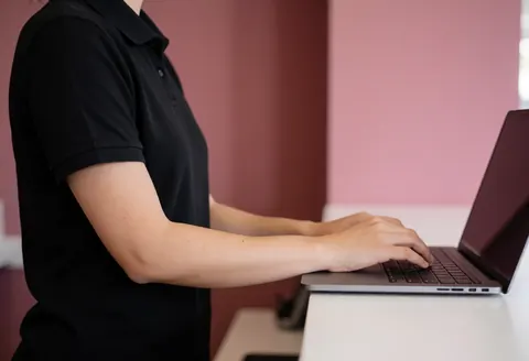 Side view of an event professional registering clients on a laptop at a counter with a pink wall background, focusing on service.