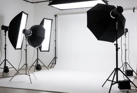 Professional video studio featuring a white curved cyclorama wall, softboxes, black umbrellas, and a tripod ready for production.