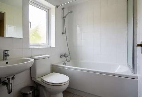 Bright residential bathroom featuring a white toilet, sink, and bathtub near a window, suitable for plumbing services