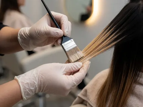 Close-up of gloved hands using a brush to apply hair dye in a salon with warm lighting and a blurred background