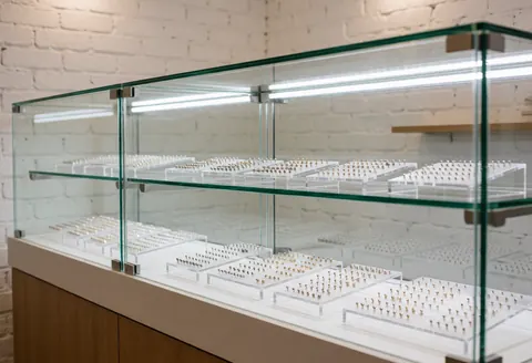 Glass display case with organized tattoo jewelry on shelves, white brick wall, professional lighting, clean and tidy environment for clients