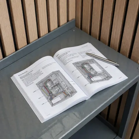 Technical dryer repair manual with electrical diagrams and a silver pen on a metal workbench against a light wood wall