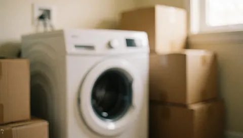 A new white washing machine sits among cardboard moving boxes in a room with warm lighting, suitable for appliance repair services.