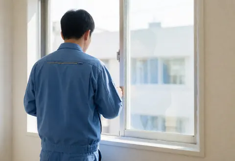 Worker in blue uniform inspects the seal of a newly installed white window in a cream office with natural light