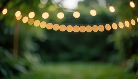 Blurred garden background with warm string lights and green foliage, ideal for outdoor event invitations and text overlays