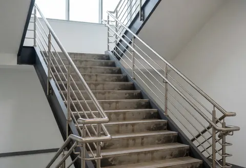 Metal office staircase with worn floors and railings, white walls, and natural light, prepared for aesthetic restoration and repair work.