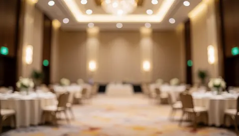 Elegant event space featuring round tables with white tablecloths, chairs, warm ceiling lights, and neutral walls, providing a clean background for text.