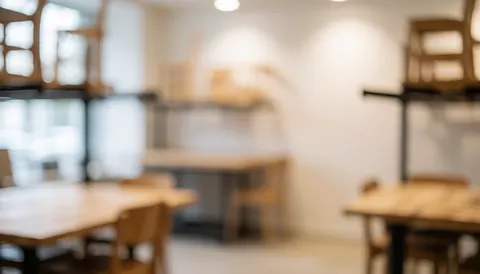 Blurred background of a furniture repair workshop with wooden tables and chairs on shelves, white walls, and warm diffused light, ideal for text overlay.