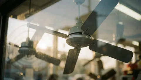 Ceiling fan inside a glass display case illuminated by warm light with a blurred background suitable for text overlay in fan repair shops