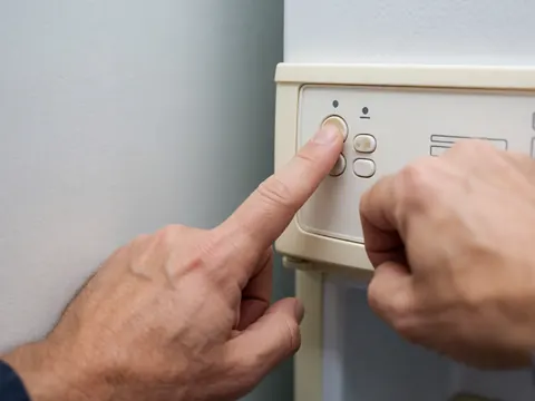 Close-up of a hand adjusting the temperature control knob on a refrigerator panel with plastic buttons against a light gray wall background
