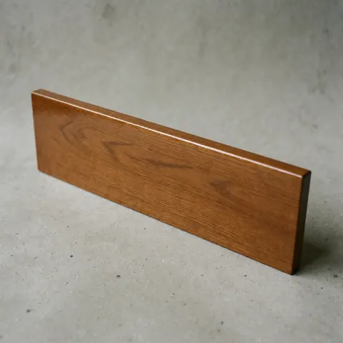 Close-up of a polished wooden drawer front with a glossy finish and visible grain texture, placed on a gray concrete background, ideal for furniture restoration products.