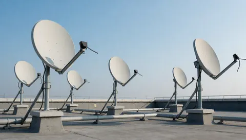 Multiple satellite dishes mounted on a concrete roof with pipes under a clear blue sky, suitable for antenna installation business backgrounds