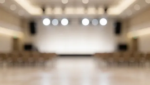 Warm blurred event background with stage lights and empty seats, ideal for text overlay, professional and calm atmosphere