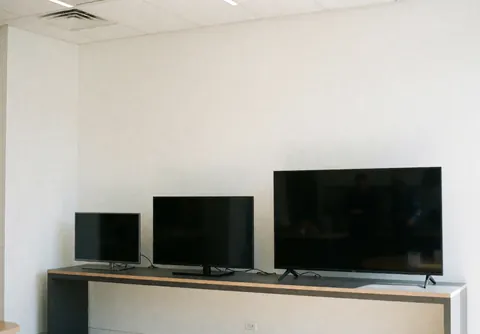 Three televisions of different sizes on a modern white counter in a clean, professional TV repair shop interior.