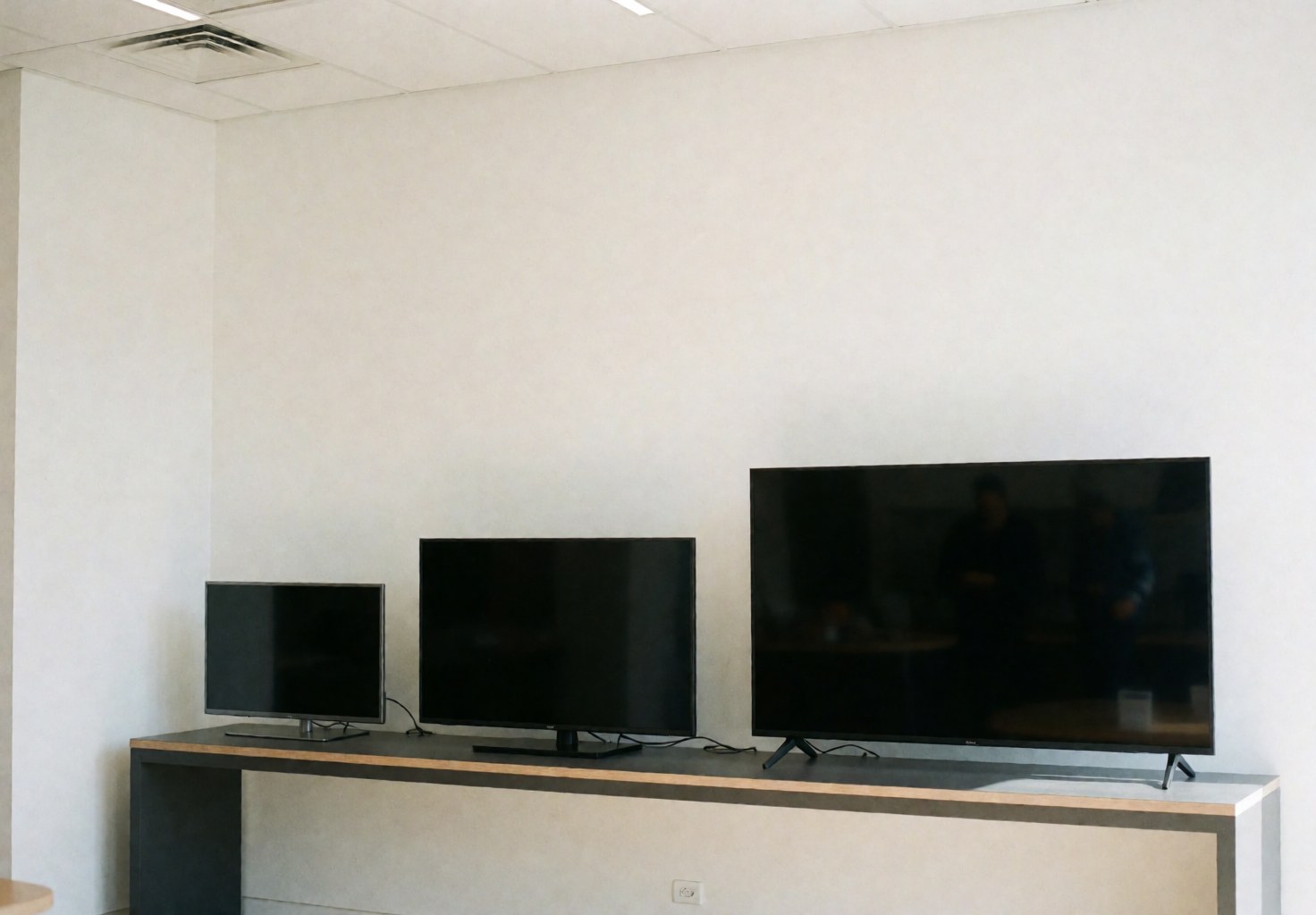 Three televisions of different sizes on a modern white counter in a clean, professional TV repair shop interior.
