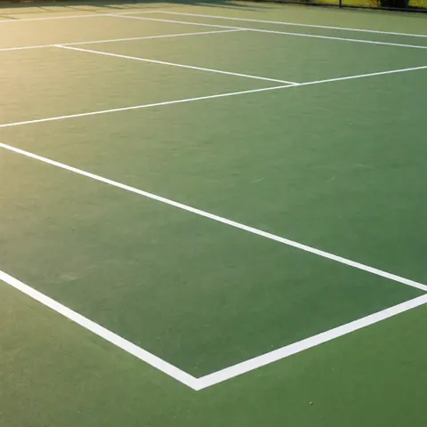 Freshly painted outdoor tennis court with green acrylic surface and crisp white lines under warm sunlight, showcasing professional installation services.