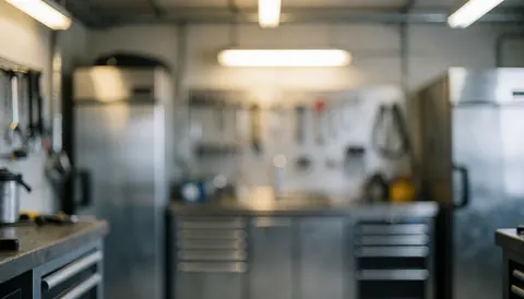 Soft focus background of a refrigerator repair shop featuring appliances, hanging tools, and metal drawers under warm lighting