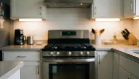 Modern kitchen featuring a stainless steel gas stove and white cabinets with warm lighting and a blurred background suitable for text overlay