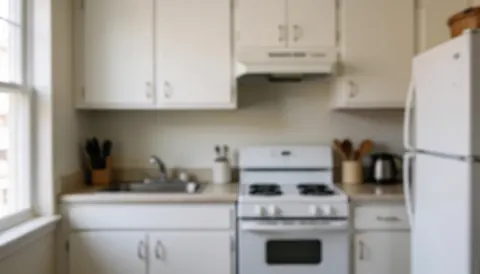 Compact kitchen featuring a white stove, refrigerator, and cabinets with a soft blurred background suitable for appliance repair services