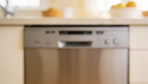 Soft focus background of a built-in dishwasher in a clean kitchen with warm lighting, suitable for commercial text overlays.
