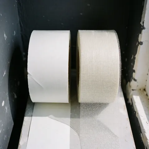 two rolls of wall repair tape, one white paper and one glass mesh, placed on a gray carbon painted wall surface