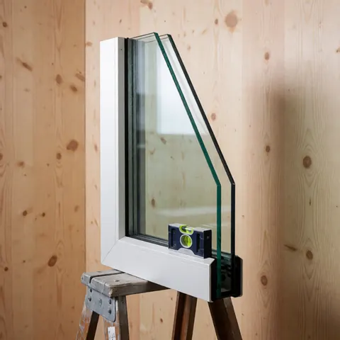 White framed insulated double glazing window with a leveler resting on a wooden ladder against light wood panel walls under professional lighting