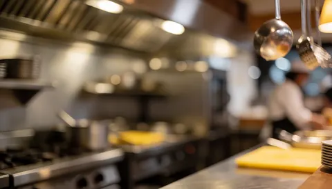 Background of a restaurant kitchen with hanging utensils, stoves, and warm light, ideal for commercial text.