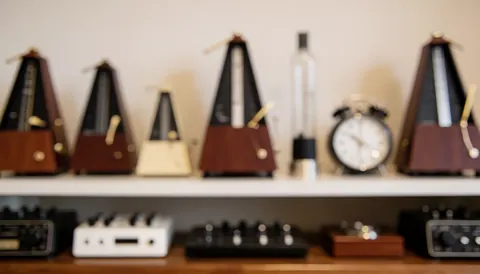 A wooden shelf holding metronomes, clocks, and musical accessories with a warm bokeh background for rhythm and discipline text.