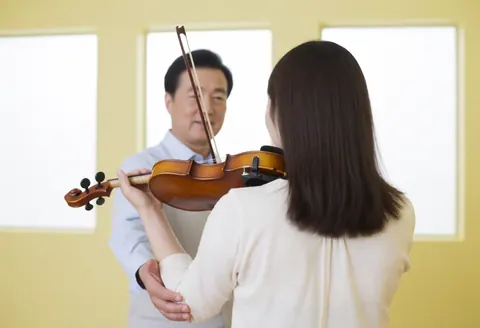 Music instructor assisting a student with proper violin holding technique in a bright, professional classroom setting
