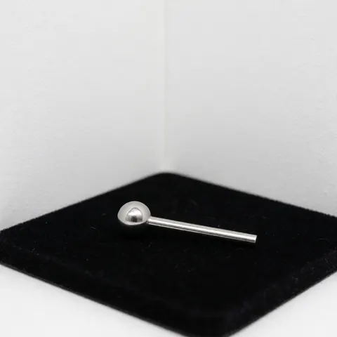 Close-up of a stainless steel ball piercing resting on black velvet with subtle reflections, isolated on a white corner for product display.