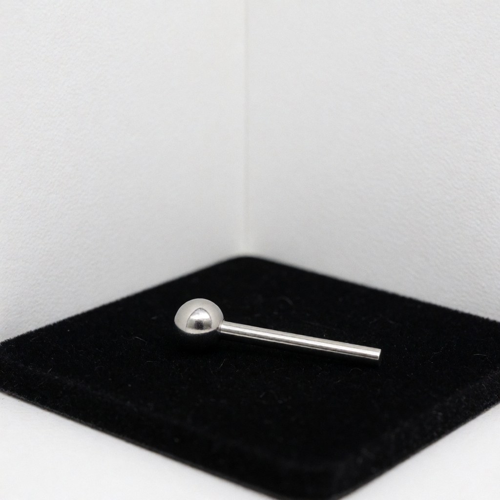 Close-up of a stainless steel ball piercing resting on black velvet with subtle reflections, isolated on a white corner for product display.