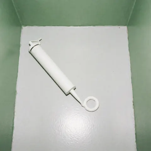 Unapplied white silicone sealant tube resting on a smooth gray surface with green walls in the background and clean lighting.