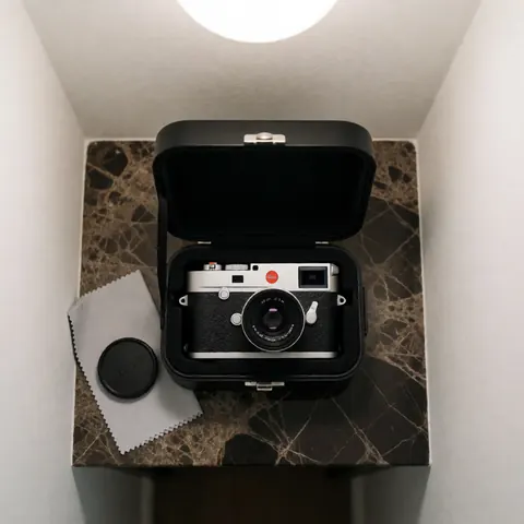 Leica M11 camera in a black case placed on a dark marble surface with a cleaning cloth and lens cap under soft overhead lighting