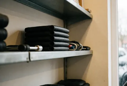 Metal shelf holding bicycle tires and locks in a clean bike workshop with cream walls and natural window light