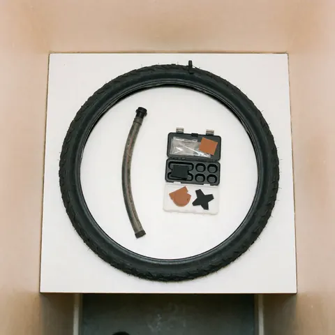 A repaired bicycle tire alongside a patch repair kit and tools arranged on a clean white surface for bike workshop product display