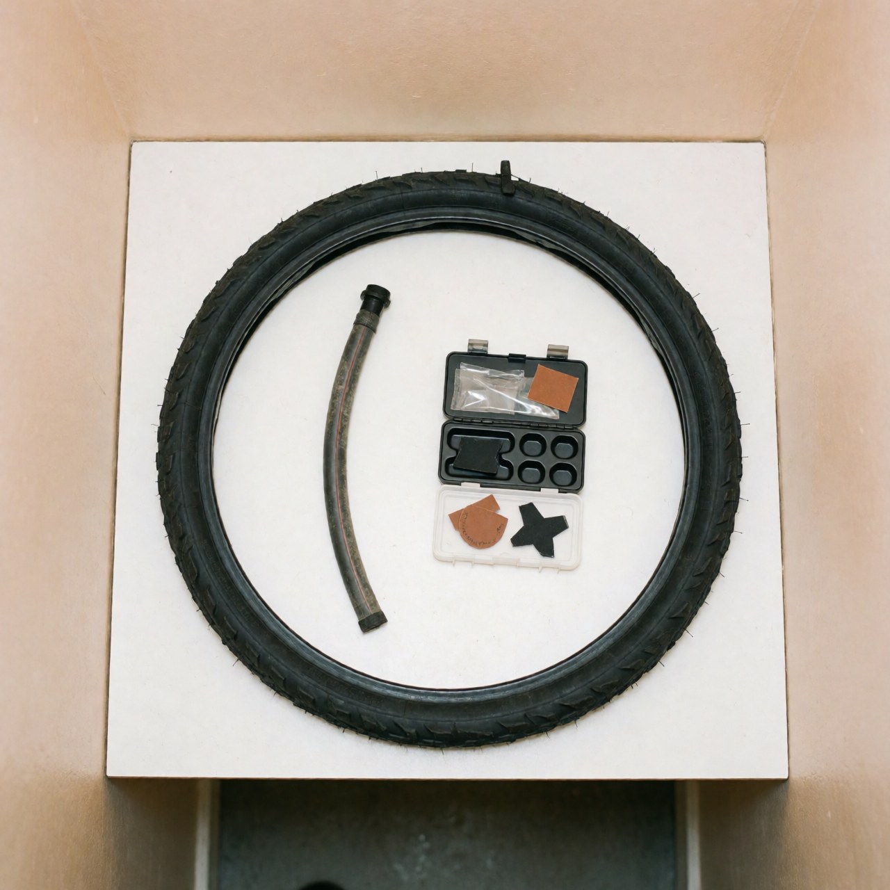 A repaired bicycle tire alongside a patch repair kit and tools arranged on a clean white surface for bike workshop product display
