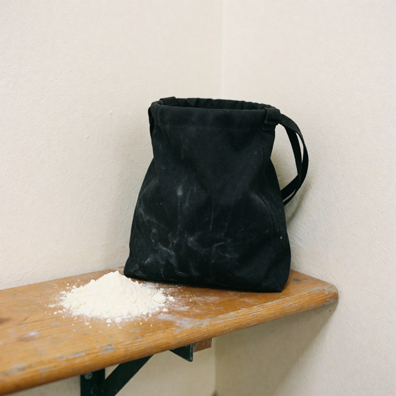 Black climbing bag with white chalk on wooden bench, white walls, natural lighting, climbing equipment