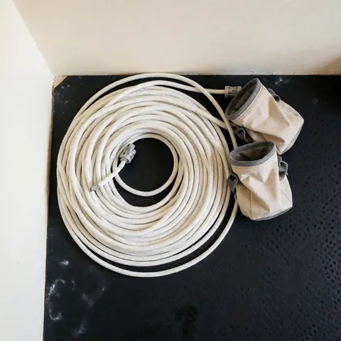 Coiled white climbing rope on a black perforated mat alongside two beige chalk bags, clean lighting for climbing centers