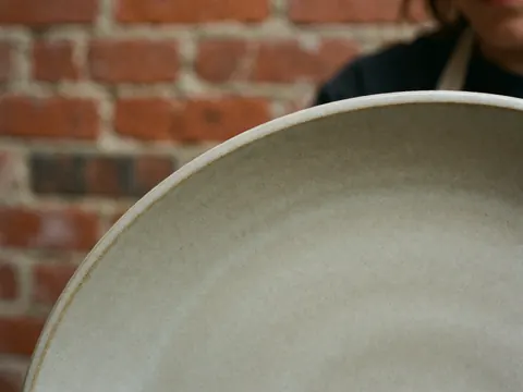 Close-up of a textured ceramic plate edge against a red brick wall background, highlighting the rustic finish.