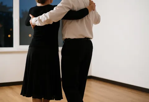 A couple dancing tango in a studio with wooden floors and soft window light, viewed from behind